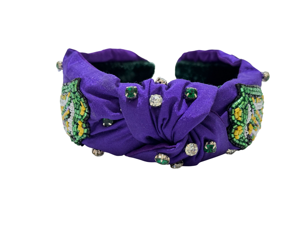 The Mardi Gras Green Tongue Beaded Knot Headband is a vibrant festival hair accessory with purple fabric, green and yellow beads, rhinestones, and green gems—perfect for making a statement against a crisp white background.