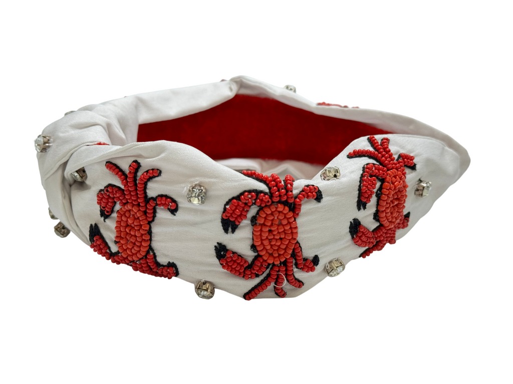 The Crab Headband is a white fabric sea life hair accessory featuring red and black beaded crab designs, small round rhinestones, and a bold red inner lining for extra color—perfect as a beach, ocean-themed statement headband.