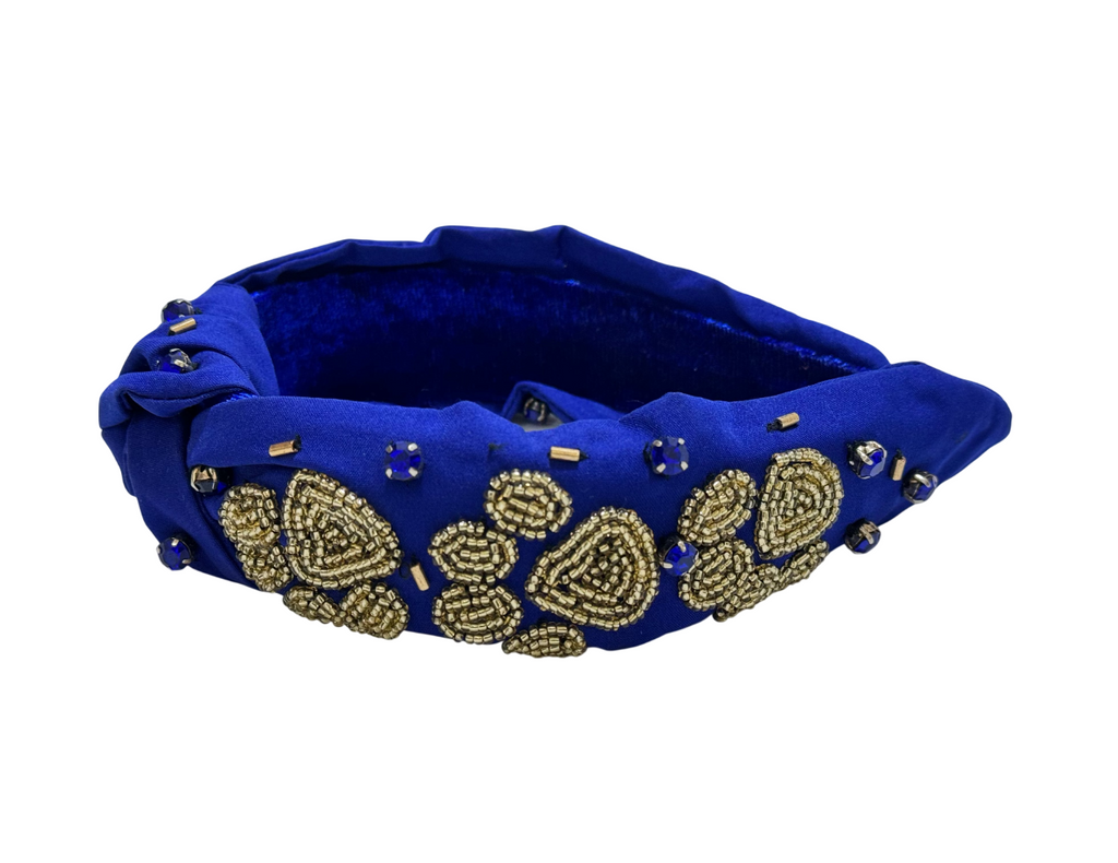 The Royal Blue Knot Headband with Gold Paw Embellishments features gold bead and sequin floral designs, blue gem accents, and a gold beaded paw—ideal for animal lovers. Shown on a white background.